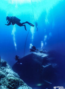 divers hovering around a crearly visible wreck on its side
